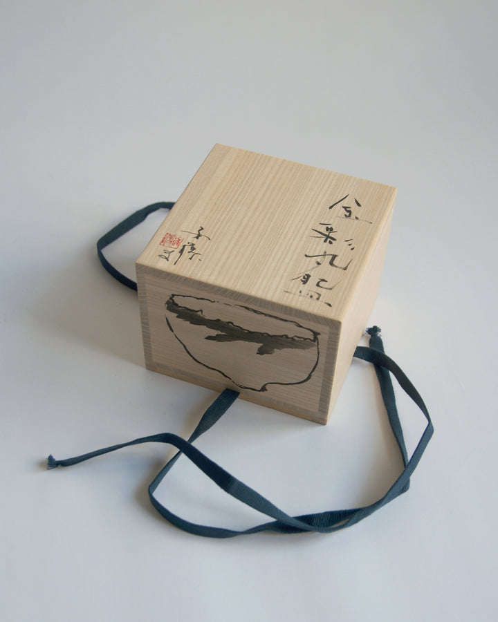 A top view of the wood box for the Gold Chawan VII. Masanobu Ando's calligraphy and drawing of the piece is shown.