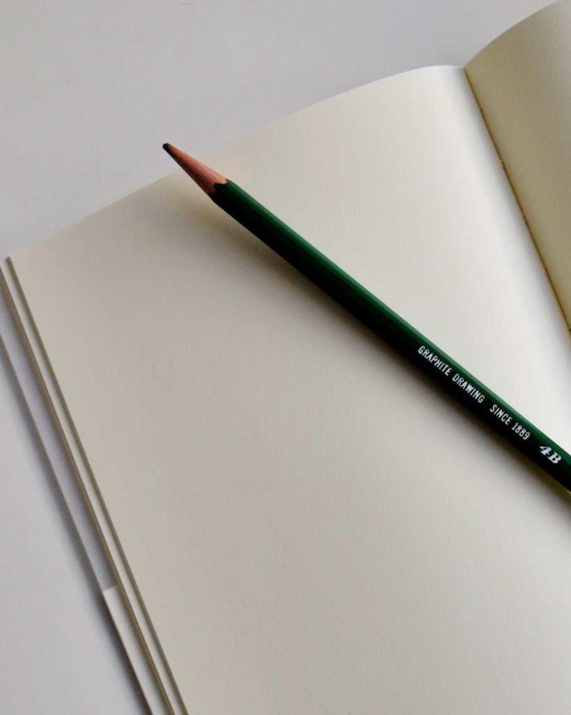 Open midori blank a5 notebook with green pencil on top.