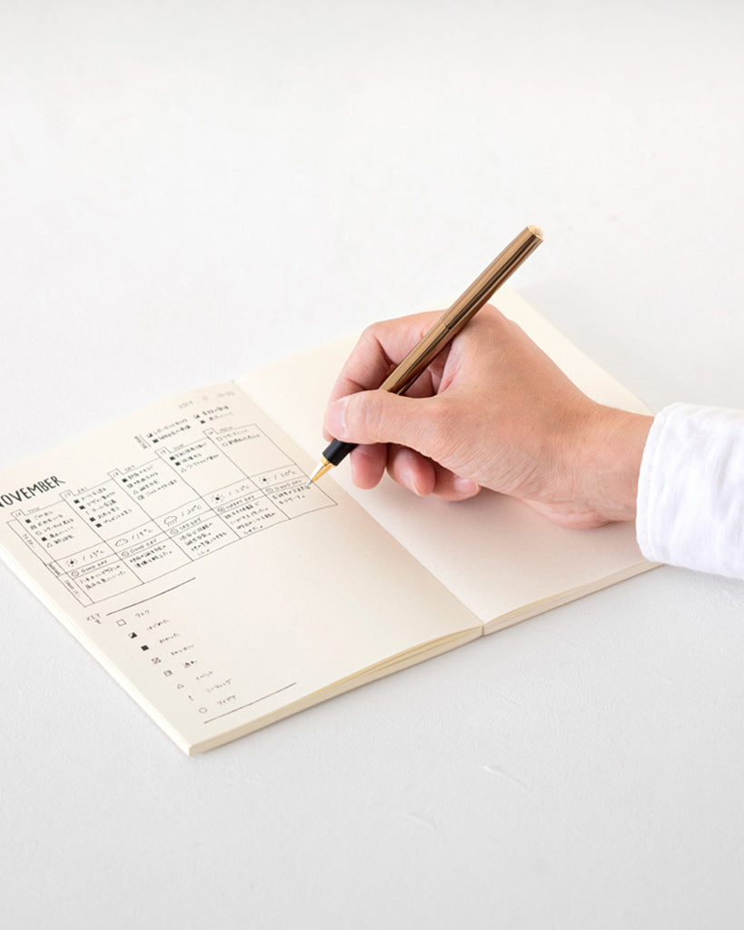 An image of a hand holding a brass pen hand writing a calendar to organize.