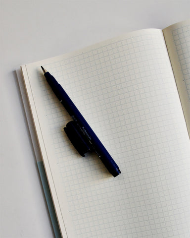 Open midori square grid a5 notebook with a navy pen on top.