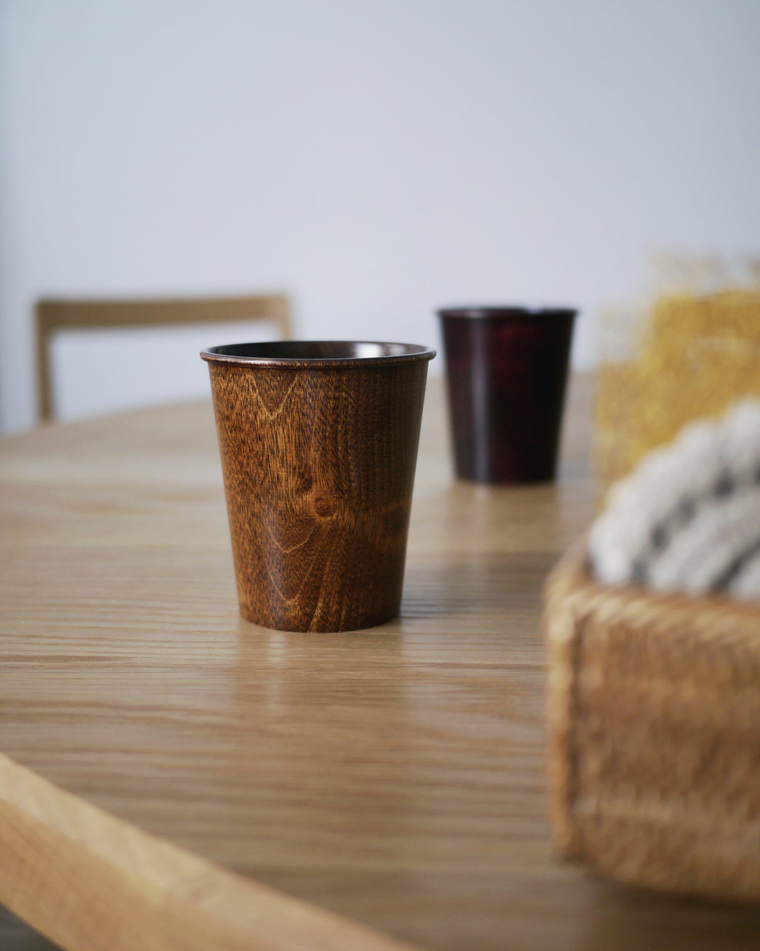 Brown urushi wood cup on a wood dining table with a red urushi wood cup blurry in the background