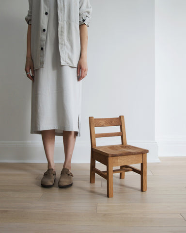A woman in gray dress and shirt standing next to the Keepsake Kids Chair.