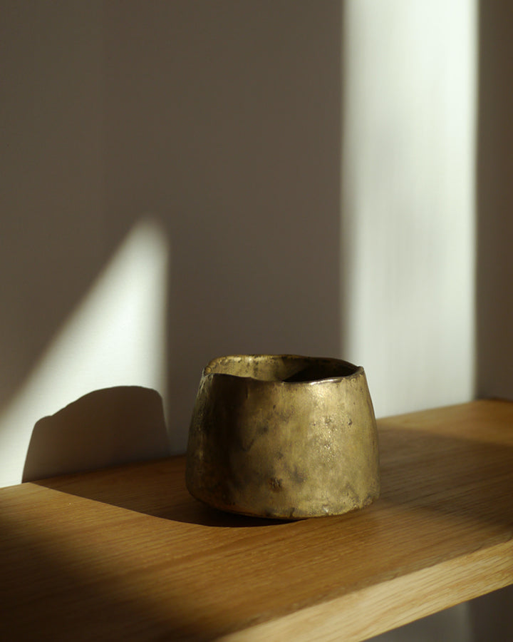 Gold Chawan on a wood shelf in natural sunlight.