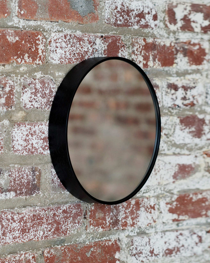 Black ash wood mirror hanging against exposed brick wall