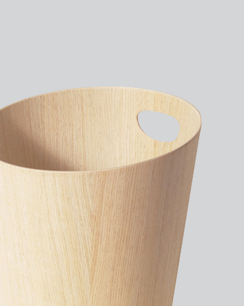 Cropped image focused on handle of white oak paper waste basket with handle by Isamu Saito against white-gray background.