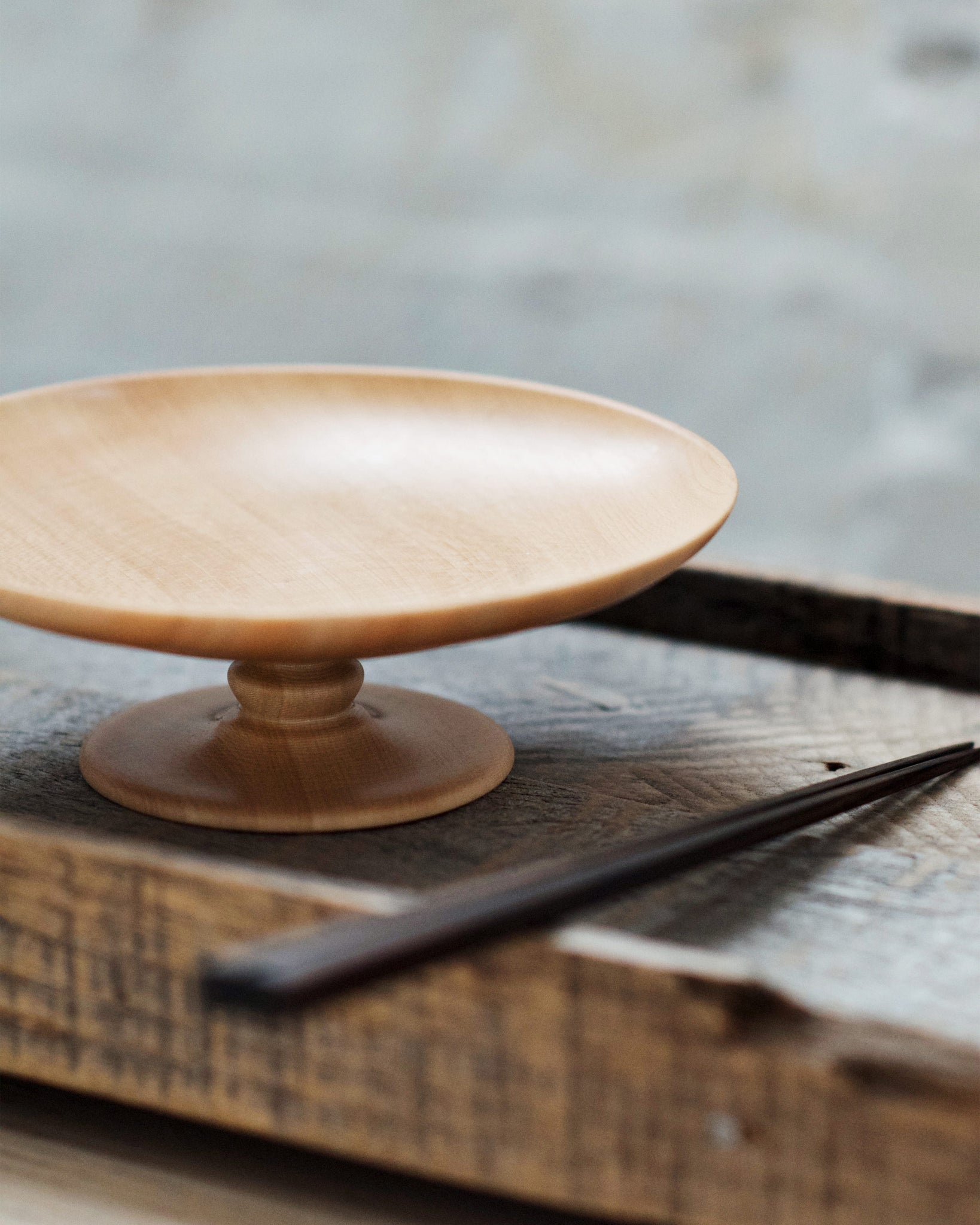 The footed plate and a pair of ebony wood chopsticks are placed on top of a dark wood tray side by side.