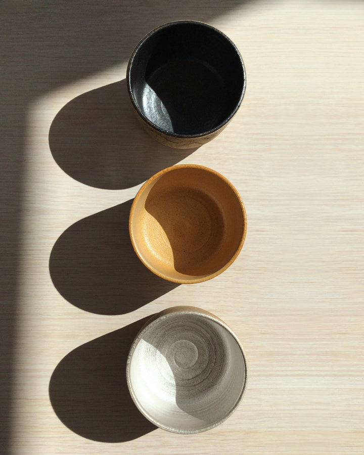 Top view of three matcha bowls in black, orange gold, and silver in a row.