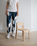 A woman in blue patchwork pants with white t-shirt standing next to hollie children's chair.