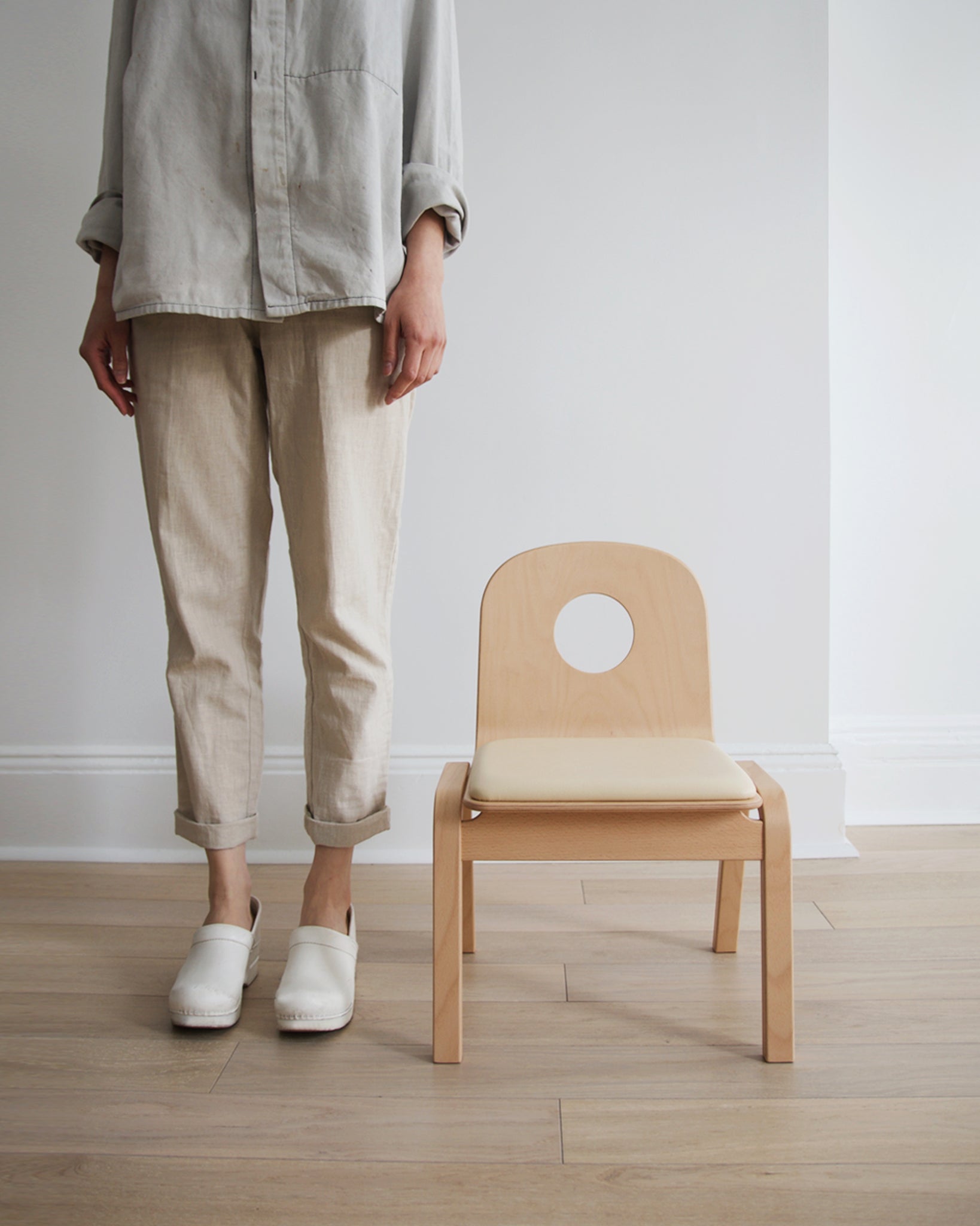 A woman in beige pants and gray shirt standing next to the Hole Children's Chair.
